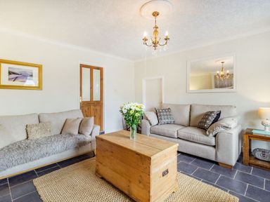 A living room with two beige sofas a wooden chest table and a chandelier at Peth Head Cottage in Wooler