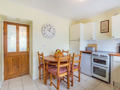 A kitchen with a wooden dining table and chairs a clock on the wall and a stove at Peth Head Cottage in Wooler