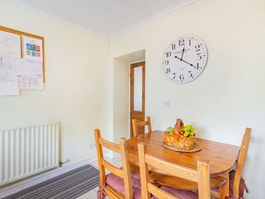 A dining area with a wooden table and four chairs a decorative fruit basket on the table a wall clock and a bulletin board on the wall at Peth Head Cottage in Wooler