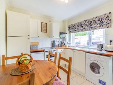 A kitchen with white cabinets wooden countertops a round wooden table with chairs and a basket of fruit at Peth Head Cottage in Wooler