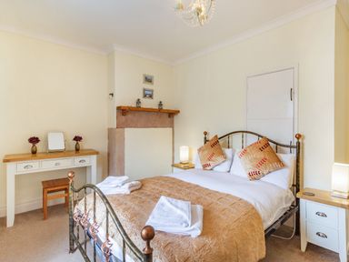 A bedroom with a double bed with pillows and folded towels a dressing table with a stool and flowers and two bedside tables with lamps at Peth Head Cottage in Wooler