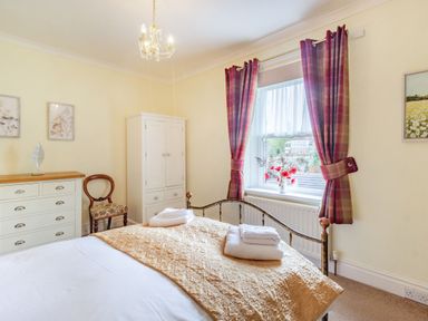 A bedroom with a bed with towels on it red curtains on the window a white wardrobe and a chest of drawers with a chair next to it at Peth Head Cottage in Wooler