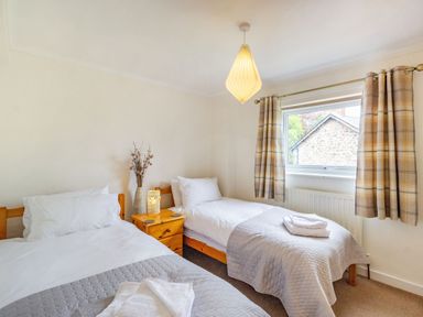 A bedroom with two single beds a wooden nightstand with a vase and a lamp a window with plaid curtains at Peth Head Cottage in Wooler