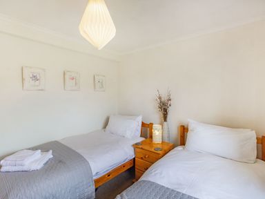 A bedroom with two single beds a wooden nightstand with a lamp and vase and three framed pictures on the wall at Peth Head Cottage in Wooler