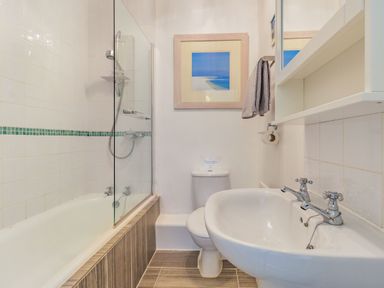 A bathroom with a bathtub shower, toilet, sink, towel rail, and framed picture at Peth Head Cottage in Wooler