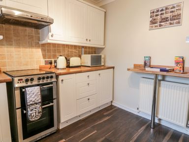 A kitchen with an electric stove oven kettle toaster microwave and a wall-mounted wooden breakfast bar at Scarborough Cottage in Driffield