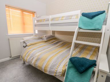 A bedroom with a white bunk bed and patterned bedding next to a window with orange blinds at Scarborough Cottage in Driffield