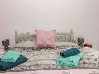 A bed with gray and white striped bedding two folded towels on top a pink pillow on the headboard two bedside tables with gray lamps and a digital clock showing 11 24 at Scarborough Cottage in Driffield