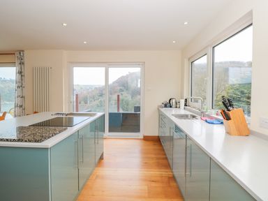 A kitchen with blue cabinets a white countertop a stovetop a sink a knife block and large windows at High Banks in Dartmouth