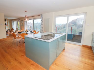 A kitchen island with stovetop and dining table with chairs near large windows showing hill views at High Banks in Dartmouth
