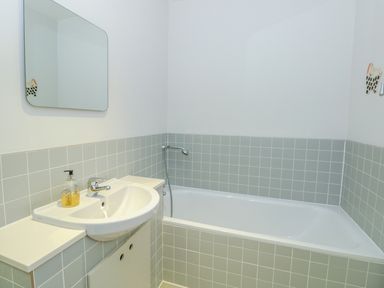 A bathroom with a white sink a mirror and a bathtub with light gray tiles at High Banks in Dartmouth
