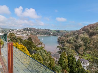 A view over a river with houses on hills and a glass balcony in the foreground at High Banks in Dartmouth