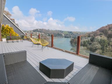 An outdoor deck with black wicker furniture and yellow chairs overlooking a river and hills at High Banks in Dartmouth