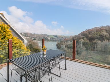 An outdoor patio with a metal table and chairs overlooking a river and trees at High Banks in Dartmouth