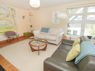 A living room with two sofas a round glass coffee table a patterned wall hanging and large windows at High Banks in Dartmouth