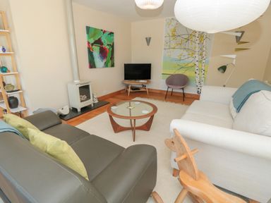 A living room with two sofas a round glass coffee table a small tv a fireplace wooden rocking horse and decorative paintings at High Banks Dartmouth