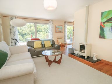 A living room with sofas a glass coffee table a wood stove and large windows showing trees outside at High Banks in Dartmouth