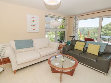 A living room with two sofas a round glass coffee table large windows and a countryside view at High Banks in Dartmouth