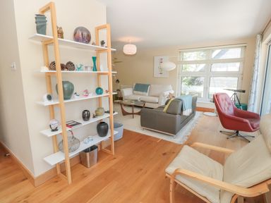 A living room with wooden shelves holding decorative items sofas a round wooden coffee table and a red chair at High Banks in Dartmouth