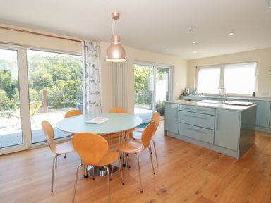 A kitchen with a round dining table and wooden chairs by large windows at High Banks in Dartmouth