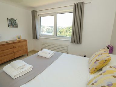 A bedroom with a bed with towels and pillows a wooden dresser and a window with curtains at High Banks in Dartmouth