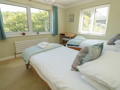 A bedroom with two single beds a desk and windows showing trees at High Banks in Dartmouth