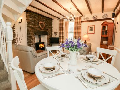 A dining area with a round table set for four and a living area with sofas and a fireplace at Dalesway Cottage in Bowness-On-Windermere