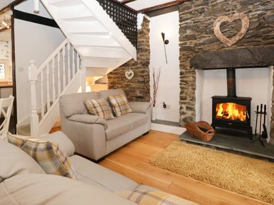 A living room with two sofas a wood burning stove and a staircase at Dalesway Cottage in Bowness-On-Windermere