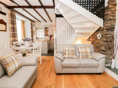 A living room with sofas and plaid pillows next to a staircase and dining table at Dalesway Cottage in Bowness-On-Windermere
