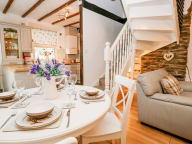 A dining table set with dishes and glasses beside a gray sofa near a white staircase and kitchen at Dalesway Cottage Bowness-On-Windermere