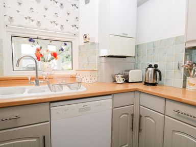 A kitchen with a sink, a dishwasher, a toaster, a kettle, and a vase with flowers at Dalesway Cottage in Bowness-On-Windermere