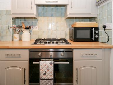 A kitchen with a gas stove oven microwave and utensil holders at Dalesway Cottage in Bowness-On-Windermere