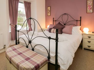 A bedroom with a metal frame bed white bedding pillows plaid bench bedside tables with lamps and curtains at Dalesway Cottage in Bowness-On-Windermere