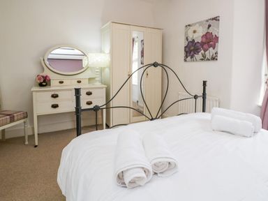A bedroom with a black metal bed frame white bedding rolled towels a white wardrobe and a white dressing table with a mirror at Dalesway Cottage in Bowness-On-Windermere