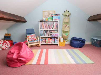 A playroom with a bookshelf filled with books and games a chair with a cushion bean bags and a striped rug at Dalesway Cottage in Bowness-On-Windermere