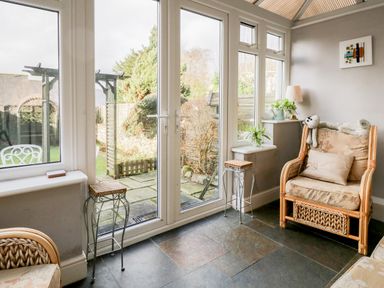 A sitting area with wicker armchairs and glass doors leading to a garden at Dalesway Cottage in Bowness-On-Windermere