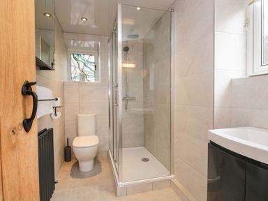 A bathroom with a shower enclosure a toilet a sink and a window with stained glass at Dalesway Cottage in Bowness-On-Windermere