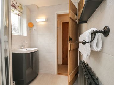 A bathroom with a sink unit a towel rack with a white towel and a wooden door at Dalesway Cottage in Bowness-On-Windermere