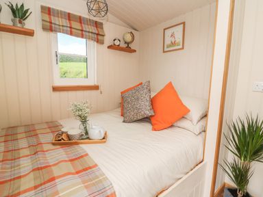 A bedroom with a bed with orange and patterned pillows and a tray with teapot and cups at Marches Way in Rhayader