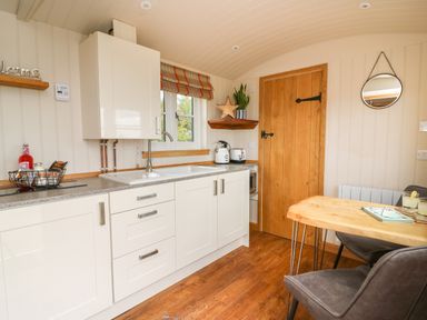 A kitchen with white cabinets a wooden door a small wooden dining table and chairs at Marches Way in Rhayader