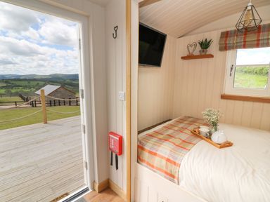 A small bedroom with a bed beside a window and an open door showing a wooden deck and countryside at Marches Way in Rhayader