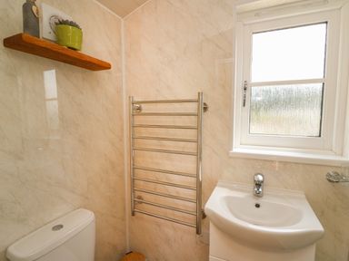 A bathroom with a toilet sink window towel rack and wooden shelf at Marches Way in Rhayader