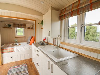 A kitchenette with a sink and window next to a small bed with cushions and shelves at Marches Way in Rhayader