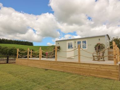 A small light green cabin with a wooden deck and rope railing in a grassy area at Marches Way in Rhayader