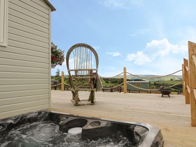 An outdoor deck with a hot tub wicker chair and wooden posts with ropes at Marches Way in Rhayader
