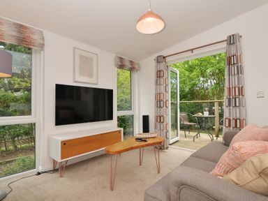 A living room with a television and access to an outdoor deck at The Hideout in Lanreath