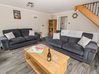 A living room with two gray sofas and a wooden coffee table with a board game and a bottle at Byefield Lodge Welland