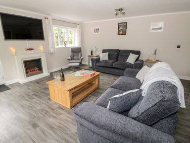 A living room with grey sofas a wooden coffee table and a TV above a fireplace at Byefield Lodge in Welland