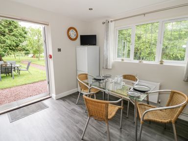 A dining area with glass table and four wicker chairs next to a window and open door to garden at Byefield Lodge in Welland