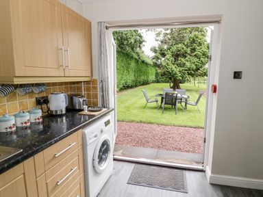 A kitchen with wooden cabinets a washing machine and a countertop leading to a garden with a table and chairs at Byefield Lodge in Welland